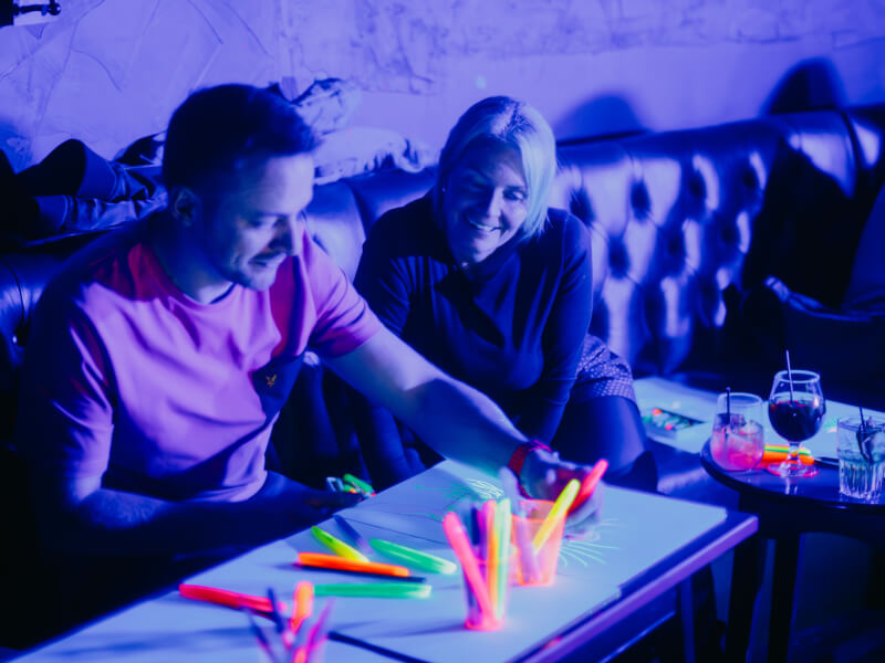 Man and woman smiling in a neon sip and paint class